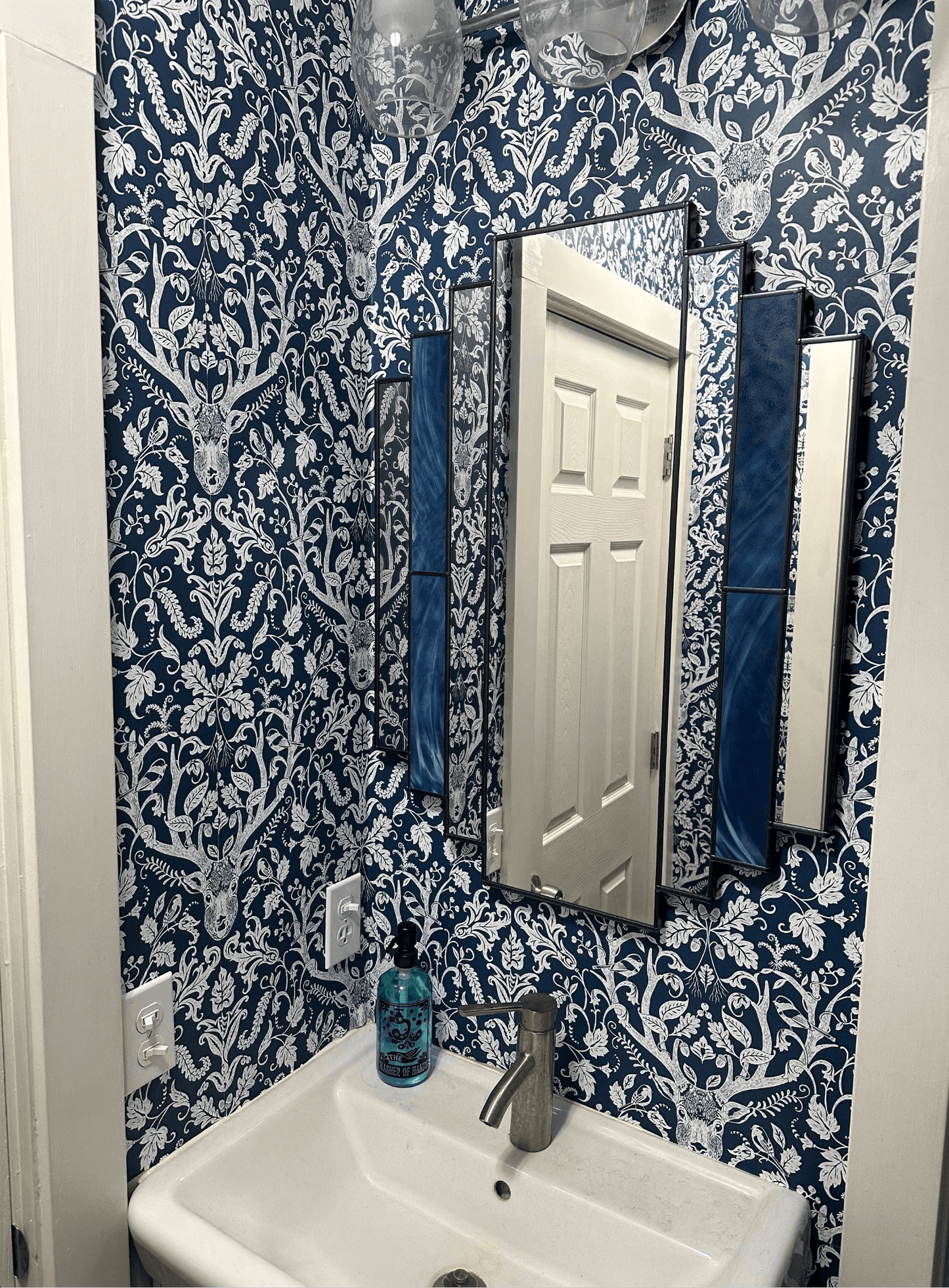 Bathroom with blue and white patterned wallpaper, sink, and mirror.