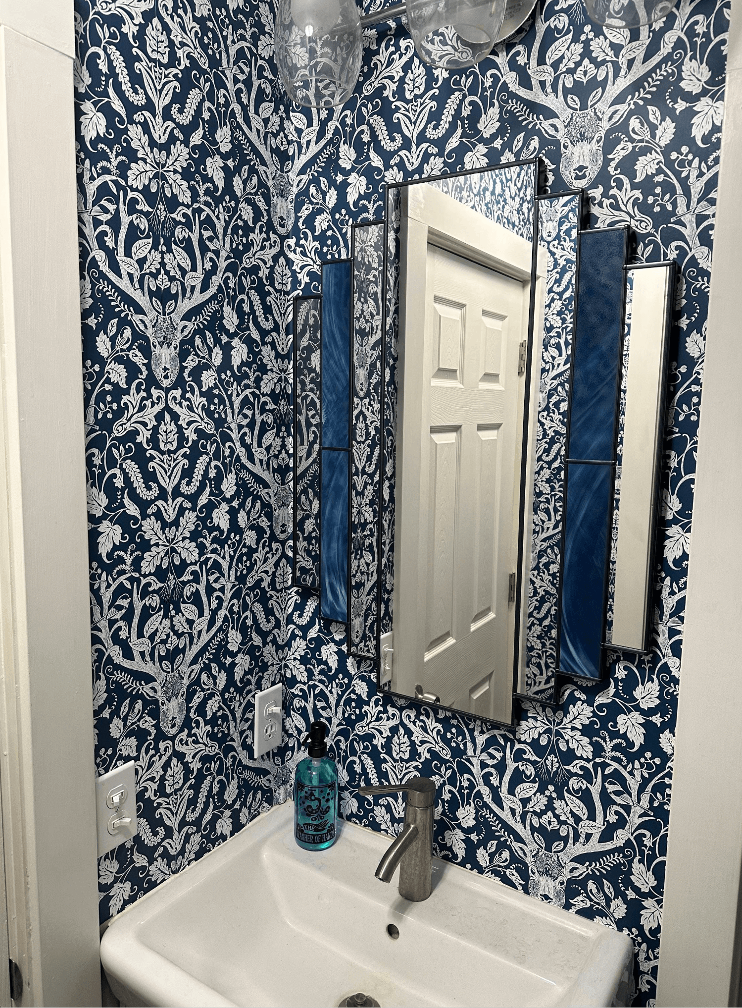 Bathroom with blue and white patterned wallpaper, sink, and mirror.