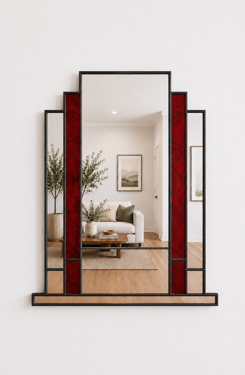 A large arched wall mirror with a black metal frame and vertical red glass panels, mounted on a white wall. The mirror reflects a modern living room interior with a sofa, coffee table, and plants.