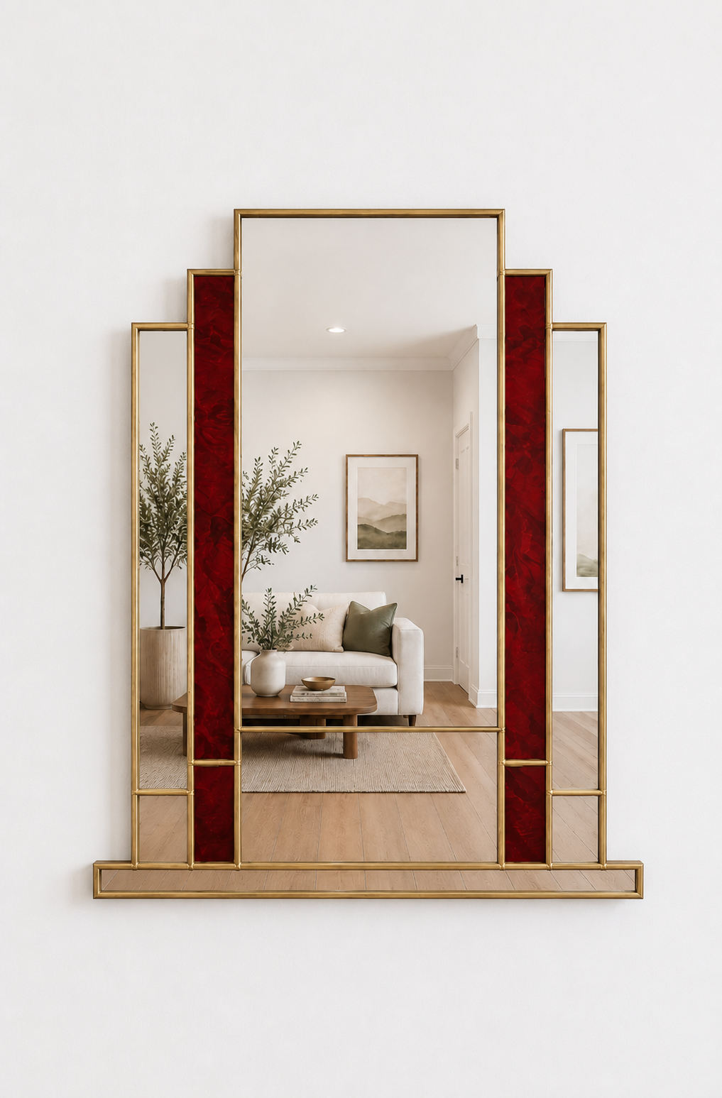 A tall rectangular wall mirror with a gold metal frame and vertical red textured side panels, mounted on a white wall. The mirror reflects a modern living room interior with a sofa, coffee table, and plants.