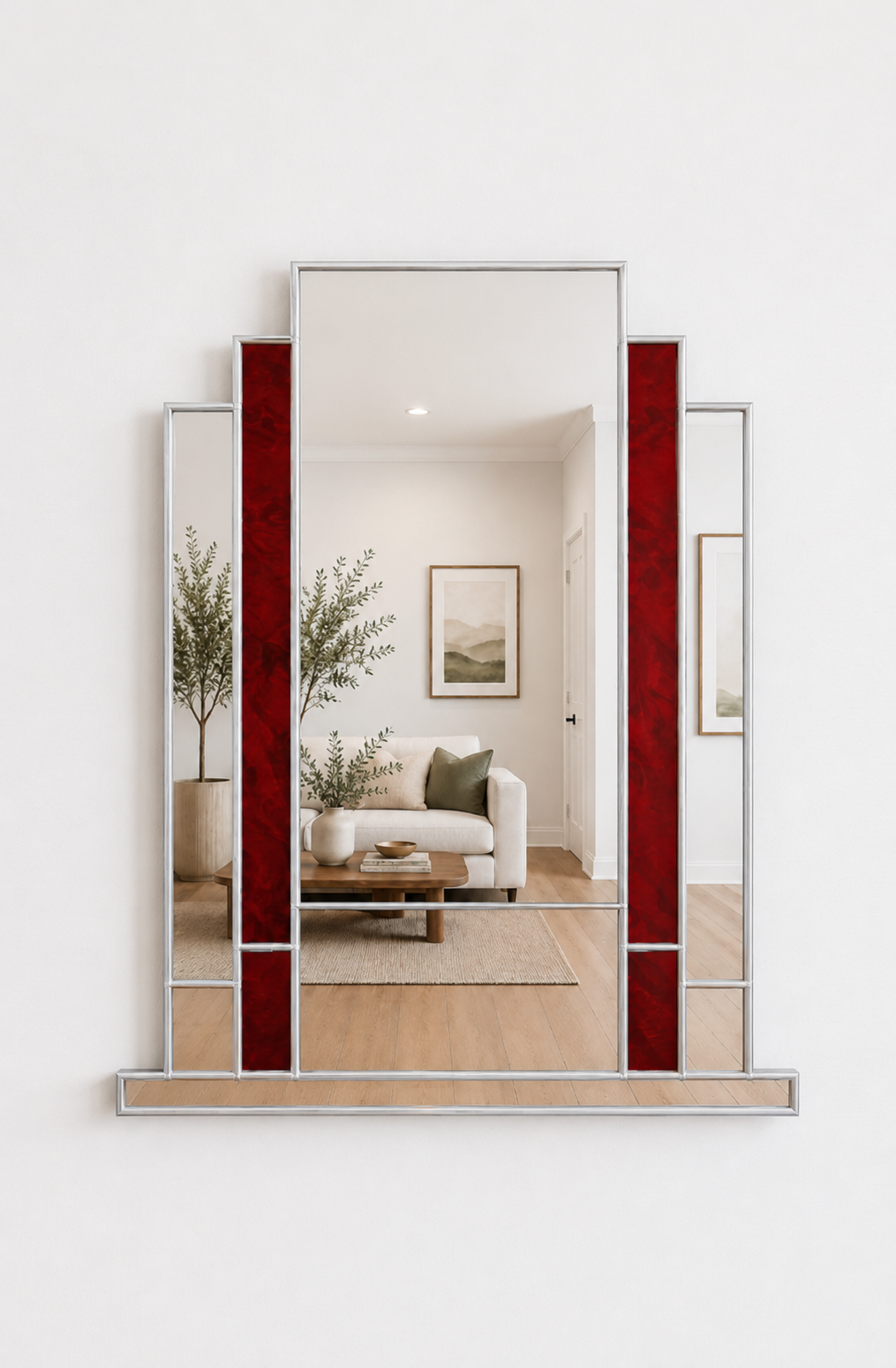 A modern geometric wall mirror with a silver frame and vertical red textured glass panels, shown mounted on a white wall with a reflection of a living room visible.