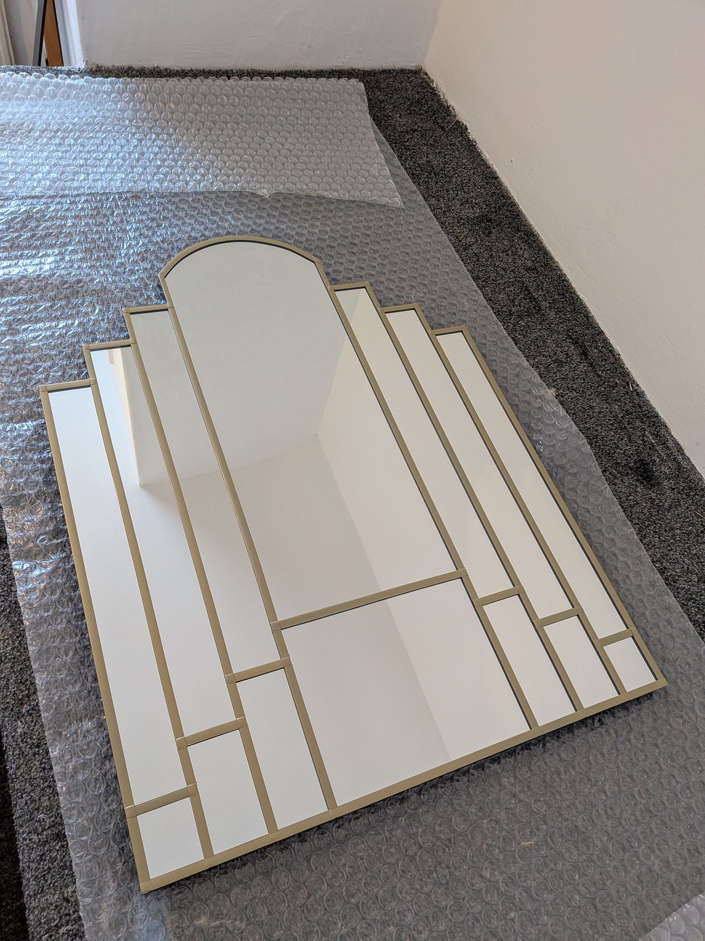 A rectangular wall mirror with an Art Deco style geometric frame in gold, resting on  bubble wrap
