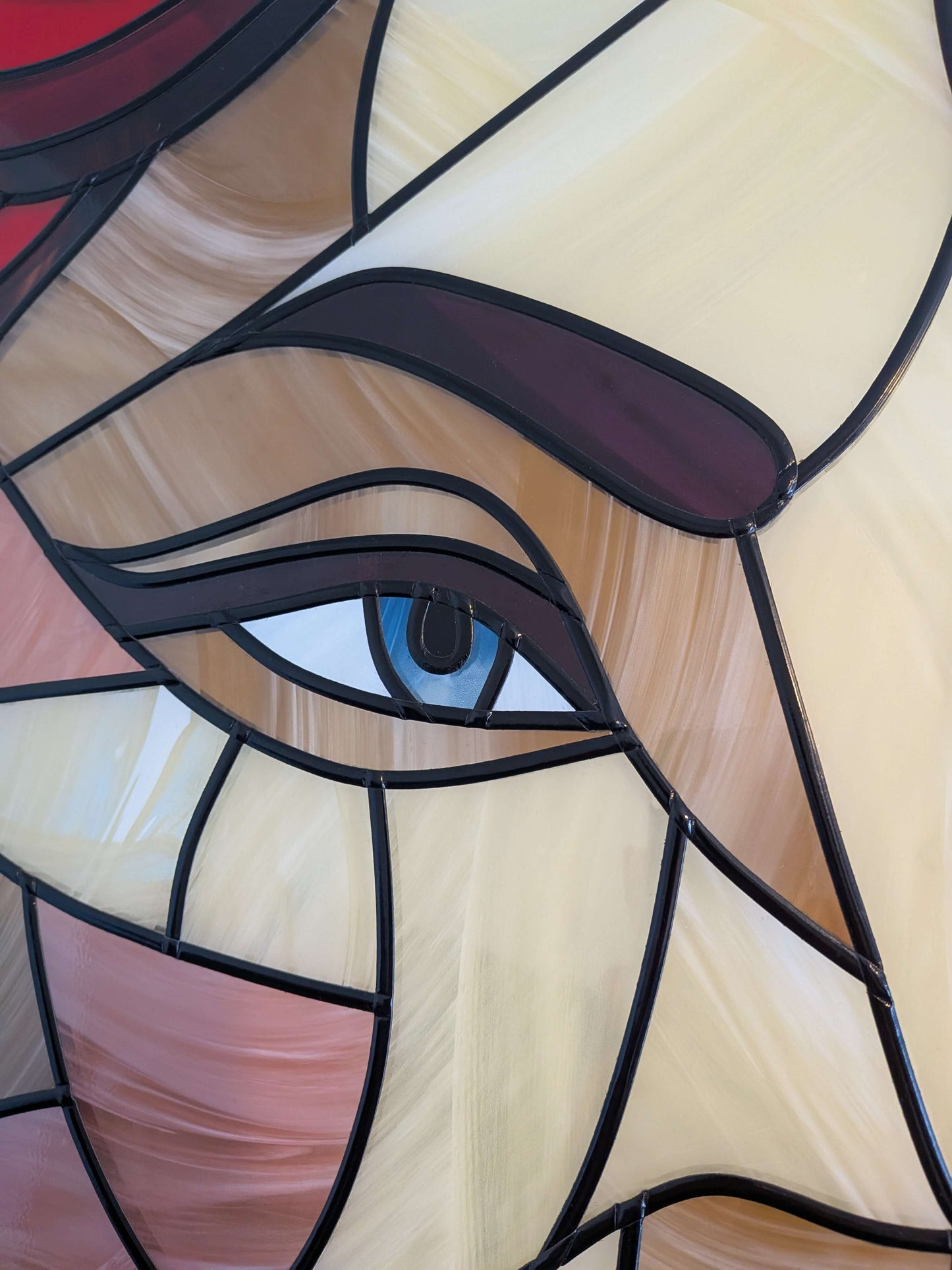 Stained glass artwork of a face with a blue eye and pink lips.